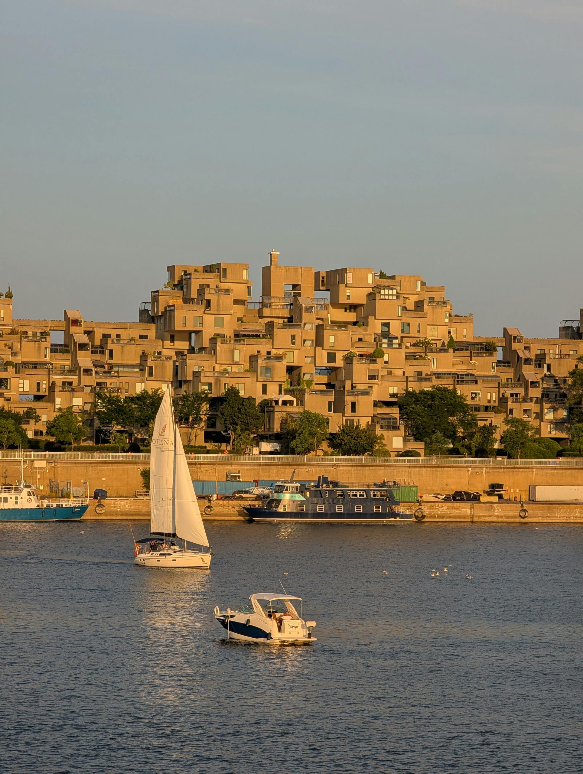 A scenic view of sailboats on the water near the iconic Habitat 67 in Montreal during a sunny day.